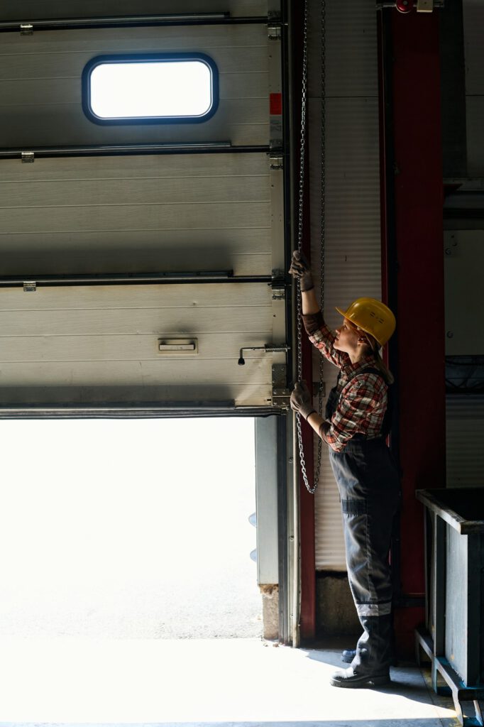 Young female engineer opening shutter roller door of garage, hangar or workshop